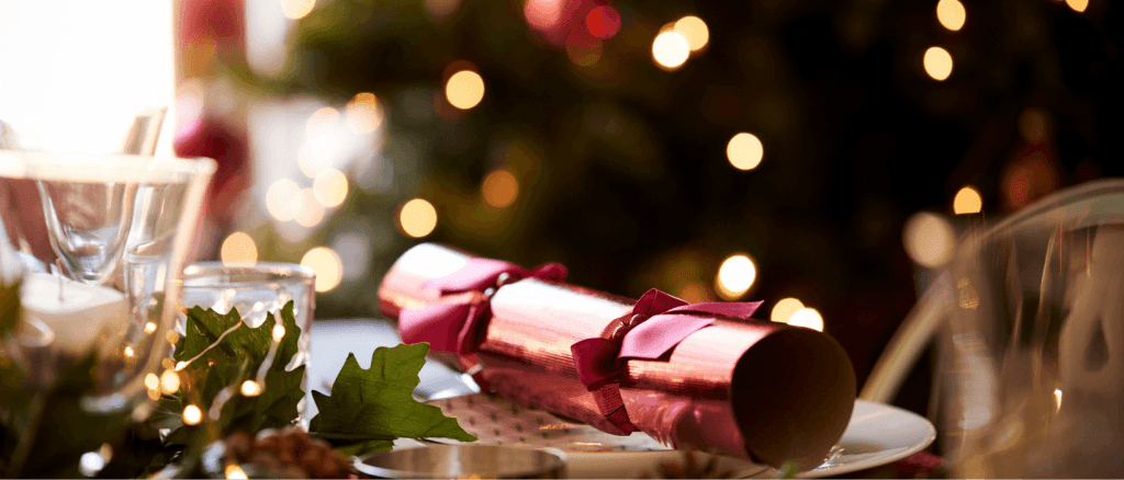 Beautiful Christmas table setting with candles and a fancy napkin on a plate with tree lights in the background.